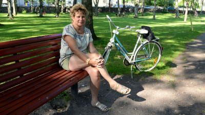 En kvinna sitter på en röd parkbänk bredvid en cykel. 