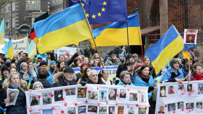 En bild på människor som går i ett demonstrationståg i Ukraina. Ukrainska flaggor syns i tåget.