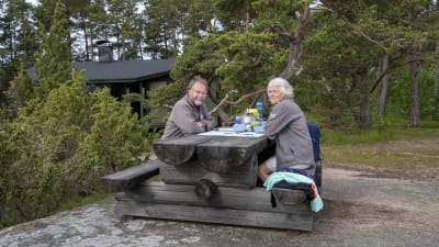 Jörgen Eriksson och Hilkka Eriksson äter morgonmål vid ett bord ute på en klippa.