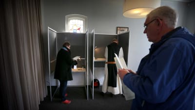 Två holländare röstar i valbås, en person köar med en valsedel i handen.