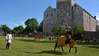 En riddare till häst och hans väpnare framför Åbo slott under ett tornerspel.
