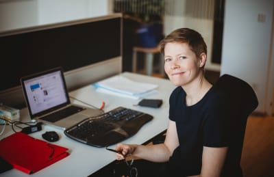 Porträtt på Heidi Hirsto. Hon sitter invid sin dator.