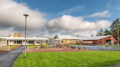 Innergården till Lauste familjerehabiliteringscenter, med en grön gräsmatta, gungor och en lekplats ingärdade av radhus.