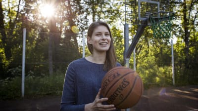 Ung kvinna med blå tröja i närbild. Hon håller i en basketboll. 