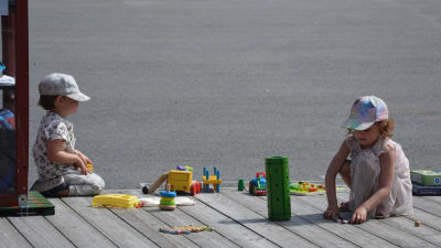 Två barn leker med leksaker på en terass.