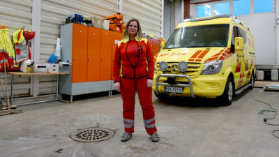 Kvinna i röda kläder står framför en ambulans.