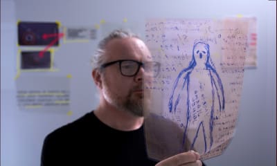 Harmaahiuksinen, silmälasipäinen mies Tommi Hakko katsoo kuvaa kädessään olevaa kuvaa avaruusolennosta.