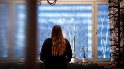 En anonym kvinna står med ryggen vänd mot kameran i ett vardagsrum.