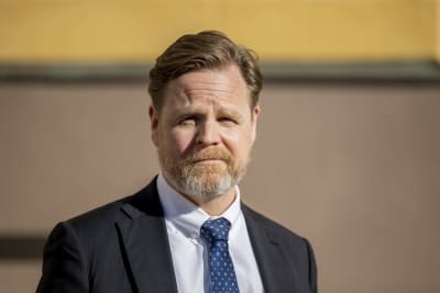Janne Kuusela i närbild mot en gul och beihe husfasad.