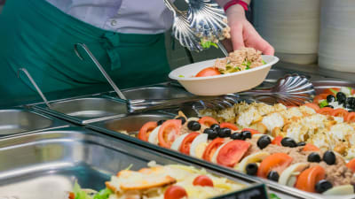 En person tar sallad ur en skolmatsbuffé.
