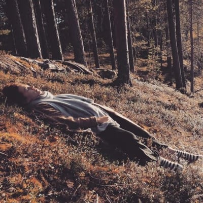 Meeri Koutaniemi makaa metsäisellä rinteellä rinteen suuntaisesti kauniina keäspäivänä.