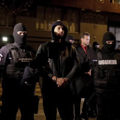 Romanian poliisit taluttavat Andrew Tatea käsiraudoissa kadulla pidätyksen jälkeen.