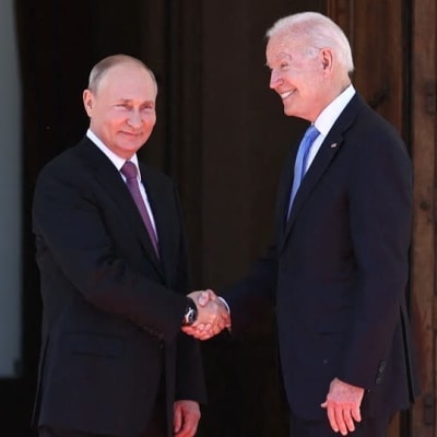 Vladimir Putin och Joe Biden skakar hand framför en stor dörr med amerikanska, ryska och schweiziska flaggor omkring sig.