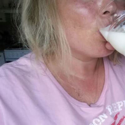 Blonditukkainen nainen juo maitoa.