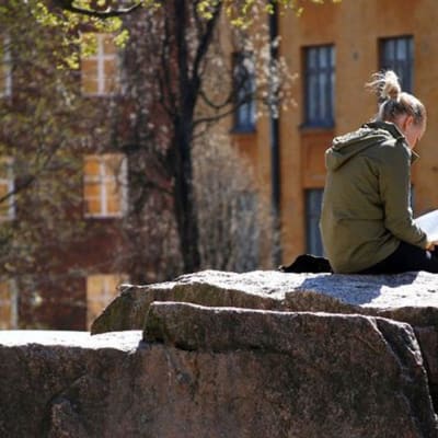 Nuori nainen lukee kirjaa kalliolla.