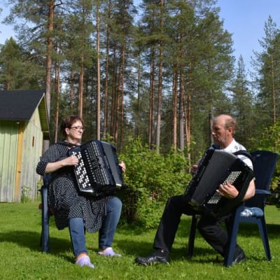 Lea Taipale ja Martti Turunen soittavat haitareita puutarhatuoleissa pihamaansa keskellä.