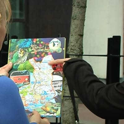 Nainen katsoo Suomen karttaa. Toisen naisen sormi osoittaa kartalla paikkaa Pohjois-Suomessa.
