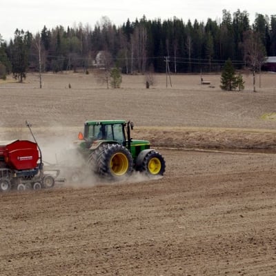 Maanviljelijä kylvää viljaa traktorilla. 