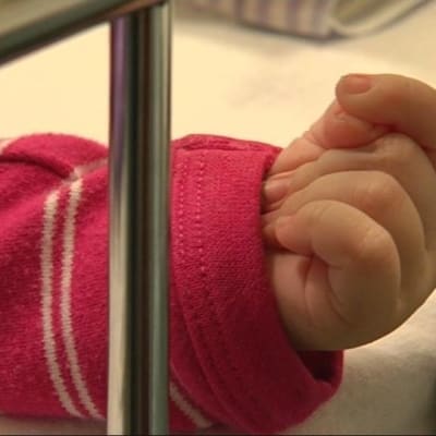 Vauvan käsi näkyy sairaalasängyn välistä.