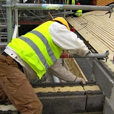 Mies työskentelee rakennustyömaalla heijastinliivi ja kypärä päällään.