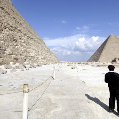 Mustapukuinen, egyptiläinen poliisimies tarkkailee pyramideja.