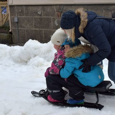 Äiti antaa vauhtia rattikelkassa istuville lapsilleen