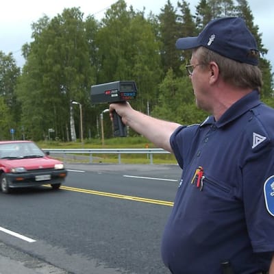 Poliisi tutka kädessä mittaamassa auton ajonopeutta