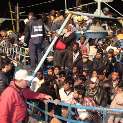 Täyteenlastattu pakolaisvene saapuu Lampedusan satamaan.