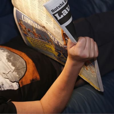 Mies makaa lukee lehteä.
