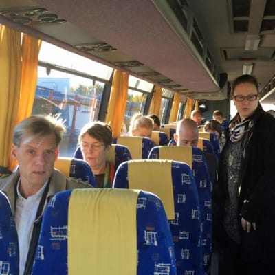 Ihmisiä, muun muassa Satu Hassi, linja-autossa.