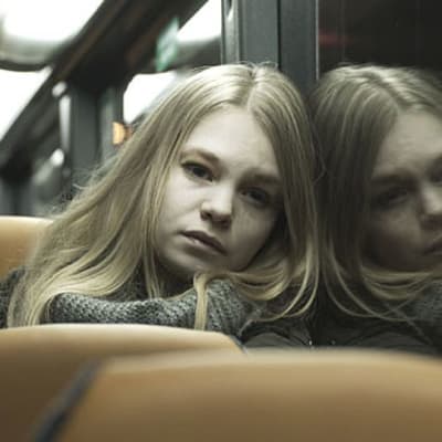 Tyttö istuu bussissa ja hänen kuvansa heijastuu ikkunasta.