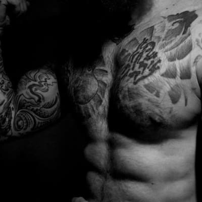 Tatuoitu mies poseeraa, kuvassa  näkyy hauista, vartalon yläosaa.