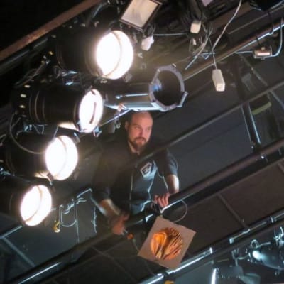 Mies säätää valoja ylhäällä katonrajassa teatterin näyttämöllä