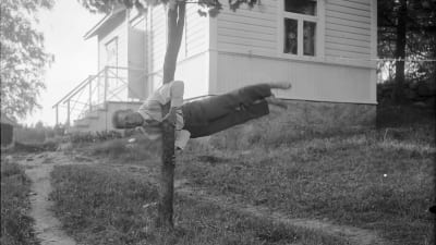 En man håller sig vågrät i luften genom att hålla fast i ett träd. Bilden är tagen 1930 i Bromarf.