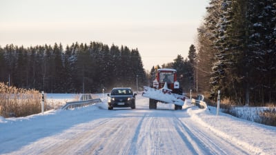 En personbil och en traktor med schaktblad möts på en isbelagd väg.