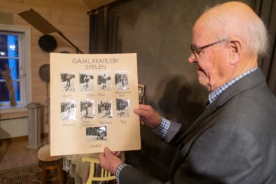 En äldre man håller upp ett plakat med foton på skidåkare.