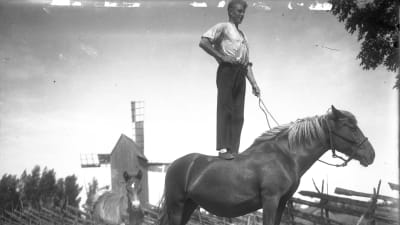 En man står på en hästrygg. Bilden är tagen 1930 i Jomala, Åland.