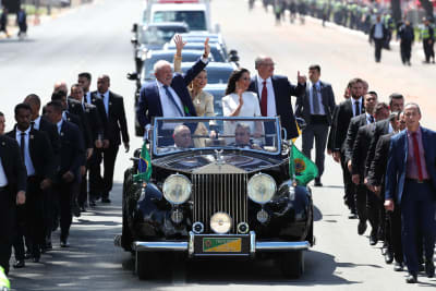 Luiz Inácio Lula da Silva och Geraldo Alckmin står och vinkar i en öppen bil tillsammans med sina fruar. På ömse sidor om bilen springer säkerhetsvakter.
