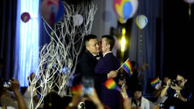 Sun Wenlin och Hu Mingliang kramas under deras bröllopsceremoni i Kina. Runt dem viftas det med regnbågsflaggor och -ballonger.
