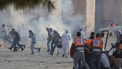 Personer omgivna av rök ocg damm springer iväg för att söka skydd under oroligheterna vid al-Aqsamoskén i Jerusalem den 27.7.2017.