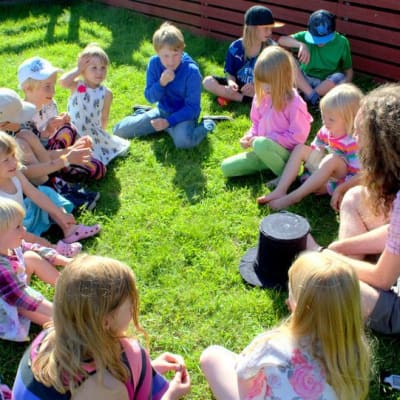 Meän Kulttuurikehdon kesäleirillä lapsia istumassa nurmikolla Seittenkaaressa.