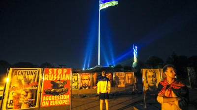 Män står vid planscher med budskap som att den ryska aggressionen mot Europa måste stoppas. I bakgrunden Ukrainas flagga.