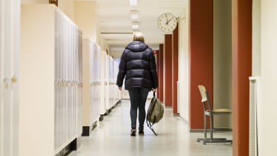 En ensam flicka med ryggen vänd mot kameran går i skolkorridor