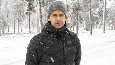 Niklas Nyman står utomhus i jacka och mössa. Det snöar ymnigt.