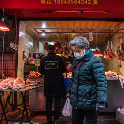 Henkilö kävelee maski kasvoillaan torilla, jossa myydään lihaa ja kalaa.