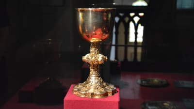 En gammal kalk för nattvard i en upplyst glasmonter i ett kyrkomuseum.