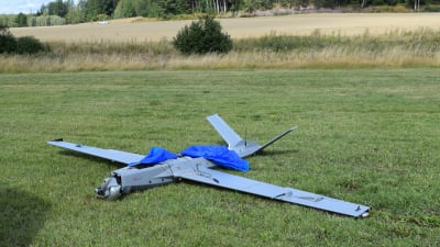 En drönare på gräset. Drönaren är av modellen som ser ut som ett litet flygplan. Den har skadats vid landningen.