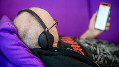 Henkilö makaa sohvalla ja kuuntelee kuulokkeet päässä kännykkä kädessään äänikirjaa.