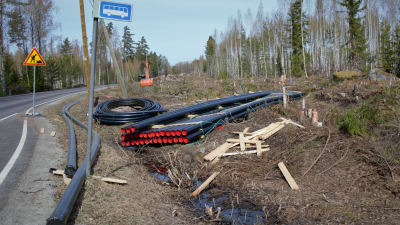 Vatten- och avloppsledningar grävs ner vid en landsväg med hjälp av en grävmaskin.