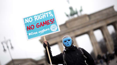 En person i blå mask protesterar mot vinter OS i Peking och Kinas behandling av Uigurer genom att hålla upp en blå skylt med texten "No Rights, No Games" framför Bradenburger Tor i Berlin. 